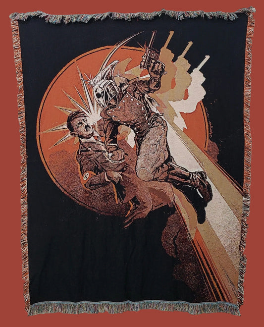 A square woven tapestry with fringe on all sides, featuring a dramatic graphic illustration of a masked figure striking another figure. The design uses a black background with a large orange circular motif, tan and brown tones, and white highlights, hanging against a plain light wall.