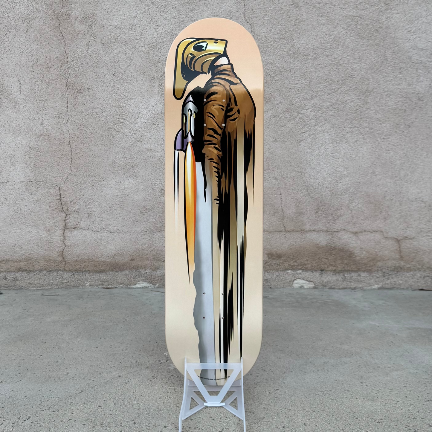 A skateboard deck with a graphic print of a bald eagle holding a spear, displayed on a small white stand against a textured concrete wall and floor. Atomic Toybox