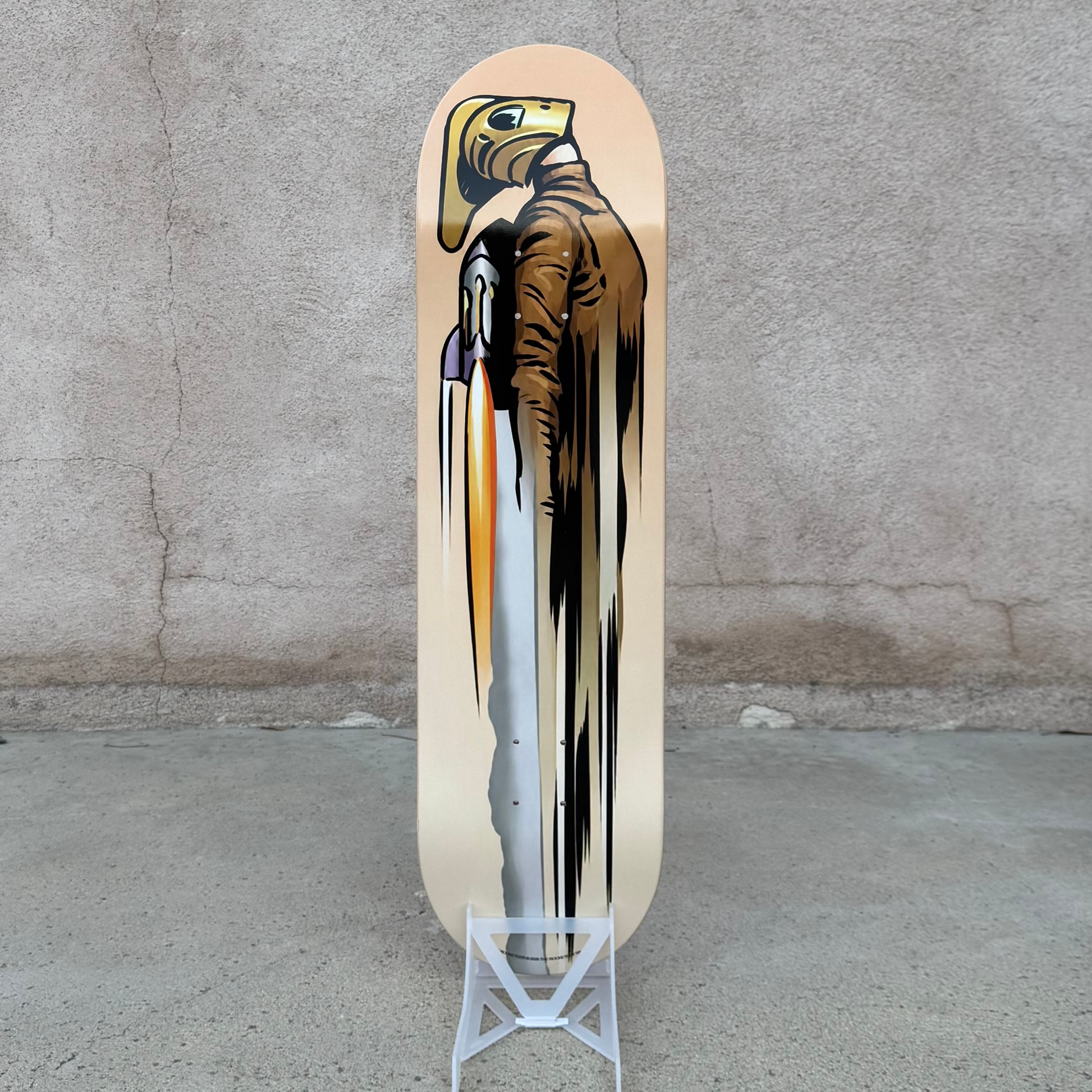 A skateboard deck with a graphic print of a bald eagle holding a spear, displayed on a small white stand against a textured concrete wall and floor. Atomic Toybox